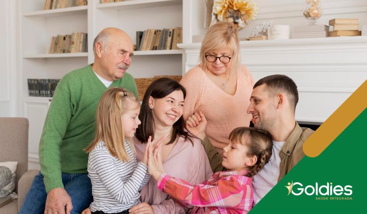 Uma família de seis pessoas, incluindo avós, pais e dois filhos, sorrindo e sentados juntos em uma sala de estar aconchegante, ilustrando o post "Terceira idade: a importância da família para os seniores"