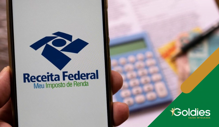Celular com o aplicativo da receita federal aberto em primeiro plano e uma calculadora ao fundo, ilustrando o post "IR: O contribuinte pode doar parte do imposto de renda para fundo de auxílio aos idosos"