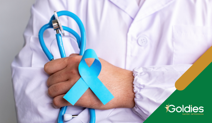 Pessoa de jaleco branco segurando um estetoscópio azul e uma fita azul de conscientização. O logotipo da Goldies Saúde Integrada está no canto.